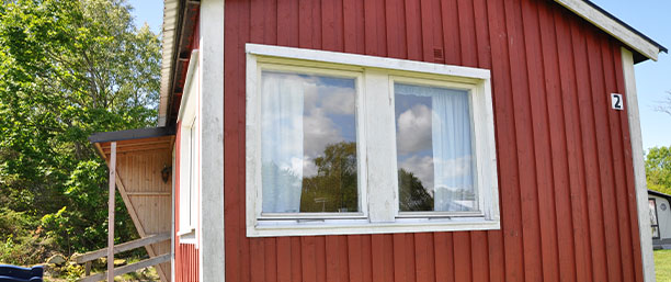 Bild på utsidan av stuga två, röd träfasad, ett stort fönster.
