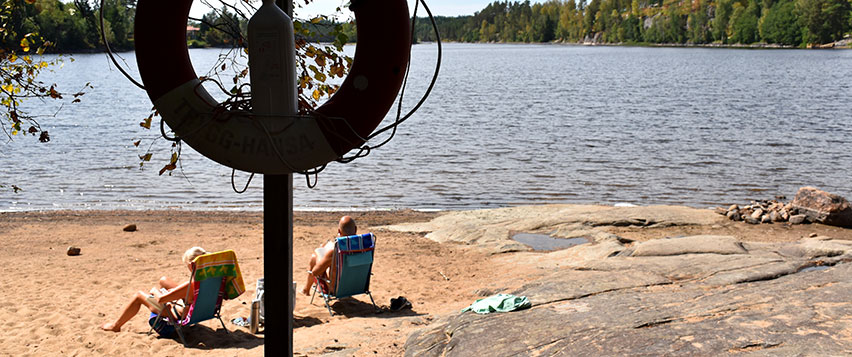 Två personer sitter i solen och läser i varsin solstol vid en sjö