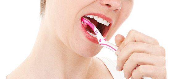 Kvinna som borstar tänder med en vit och rosa tandborste.