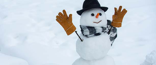 En snögubbe med morot till näsa, svart hatt och bruna handskar på pinnar till armar.