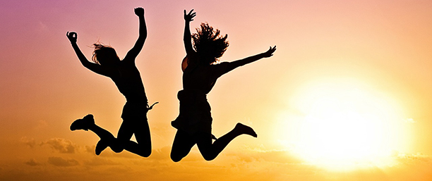 Två ungdomar hoppar högt i solnedgången.