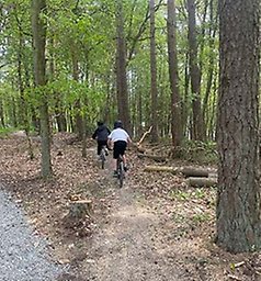 Elever i cykelhjälmar cyklar på en skogsstig.